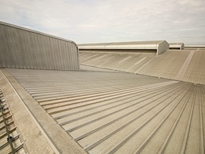 Concrete rooftop with sloped sections, ribbed panels, and a ventilation vent against a cloudy sky.