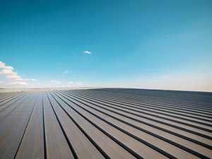 Standing-Seam-Metal-Roof-Zanesville-OH-Ohio-1 | Cosam Contracting Wide view of dark metal roof panels with parallel ridges receding toward the horizon under a clear blue sky with a few clouds.